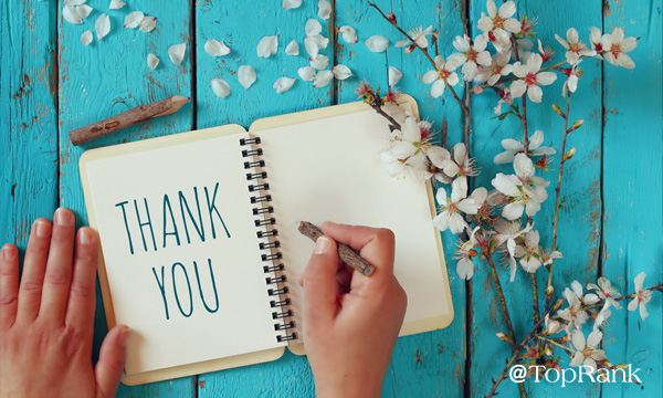 Hands writing thank you in a book surrounded by flowers image.